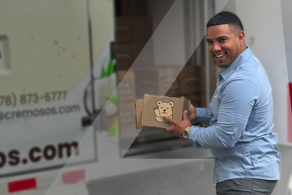 Manny from Cremosos smiling while holding product boxes in front of the branded company truck.